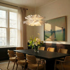 Clérachic flower chandelier hanging over a long dark wood dining table between tall curtained windows.