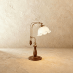 Clérachic table lamp with a ruffled milky glass shade glowing on an adjustable brass and wood arm.