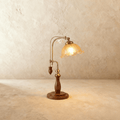 Clérachic table lamp with a fluted amber glass shade glowing warm on an adjustable brass and wood arm.