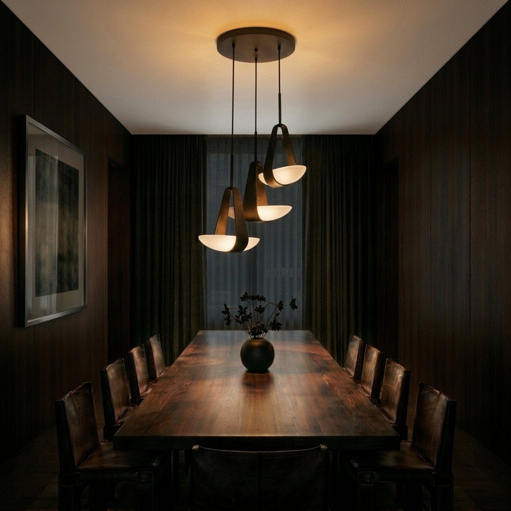 Clérachic three-shade pendant cluster lit above a long dark wood dining table lined with leather chairs in a panelled room.