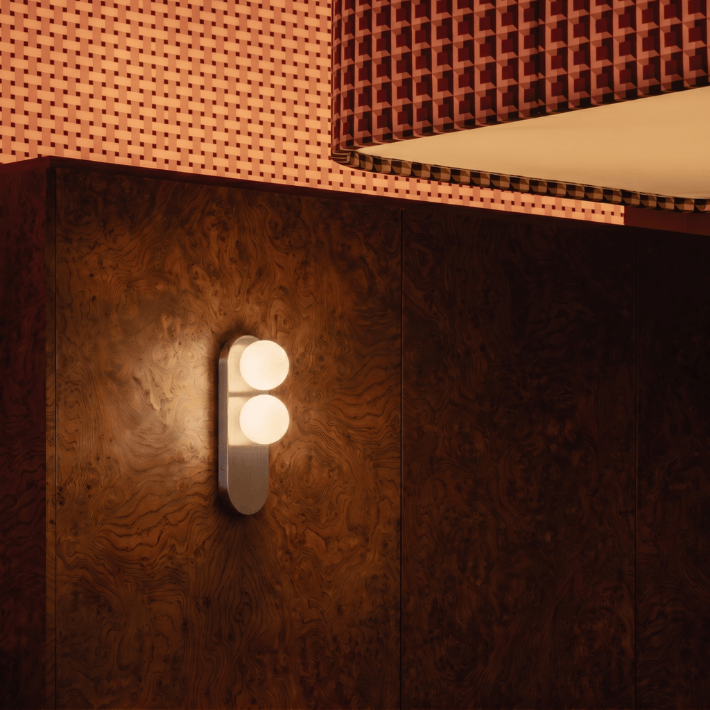 This Clérachic wall light glows against a burl-wood panel beneath a patterned upholstered headboard.