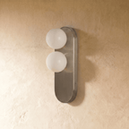 A Clérachic wall light stacks two round glass globes on a brushed nickel backplate against a plaster wall.