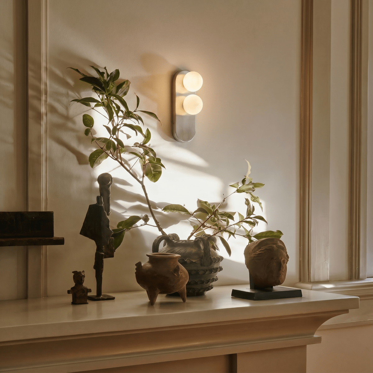 This Clérachic wall light glows above a mantel styled with small sculptures and a leafy branch.