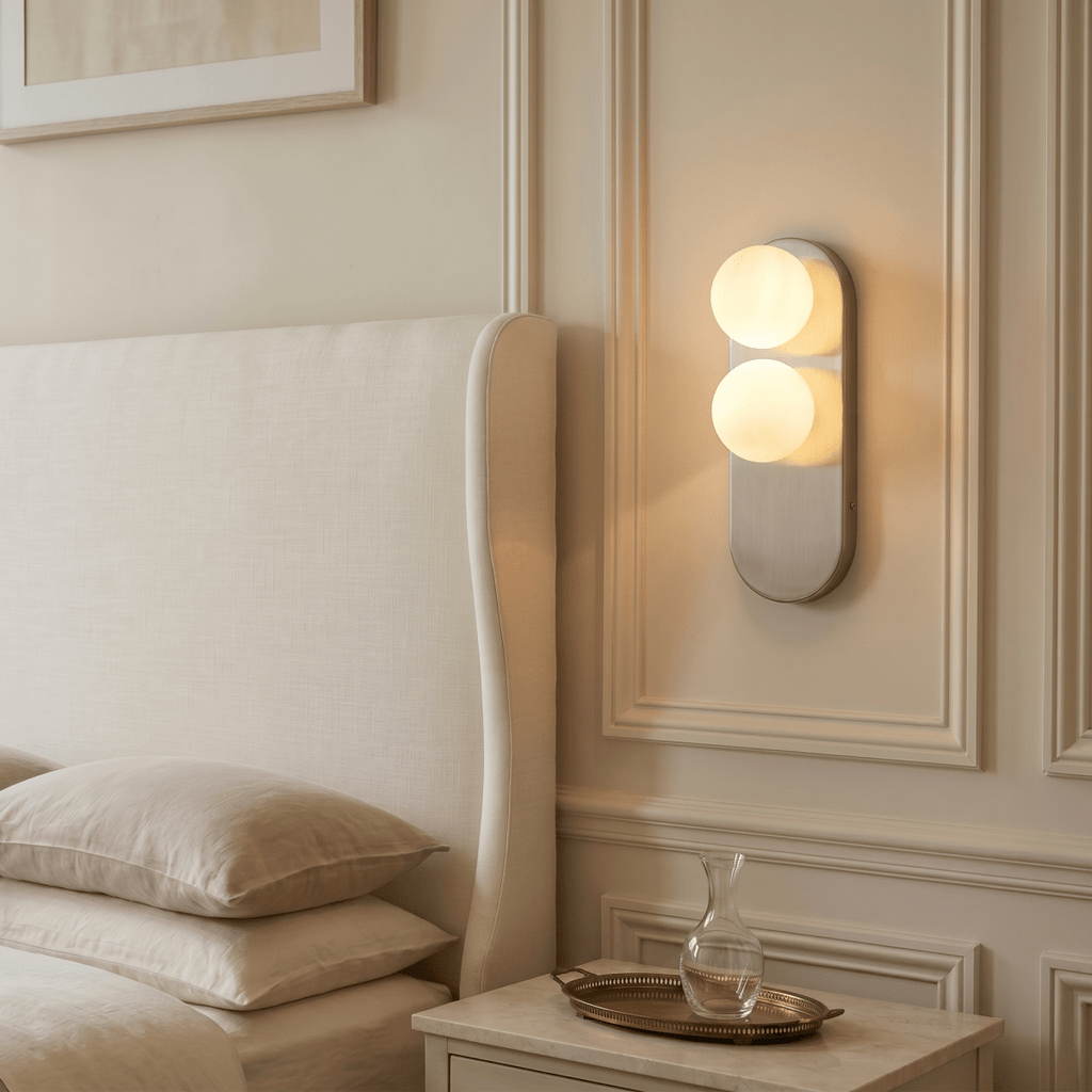 This Clérachic wall light glows warmly beside an upholstered headboard, lighting a marble bedside table.