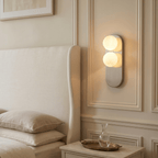 This Clérachic wall light glows warmly beside an upholstered headboard, lighting a marble bedside table.