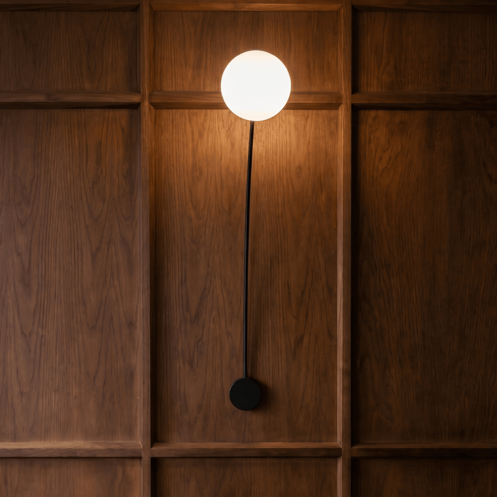 Clérachic curved wall lamp in matte black on a warm wood-panelled wall, the arm running almost straight up to a globe set directly above the wall plate.
