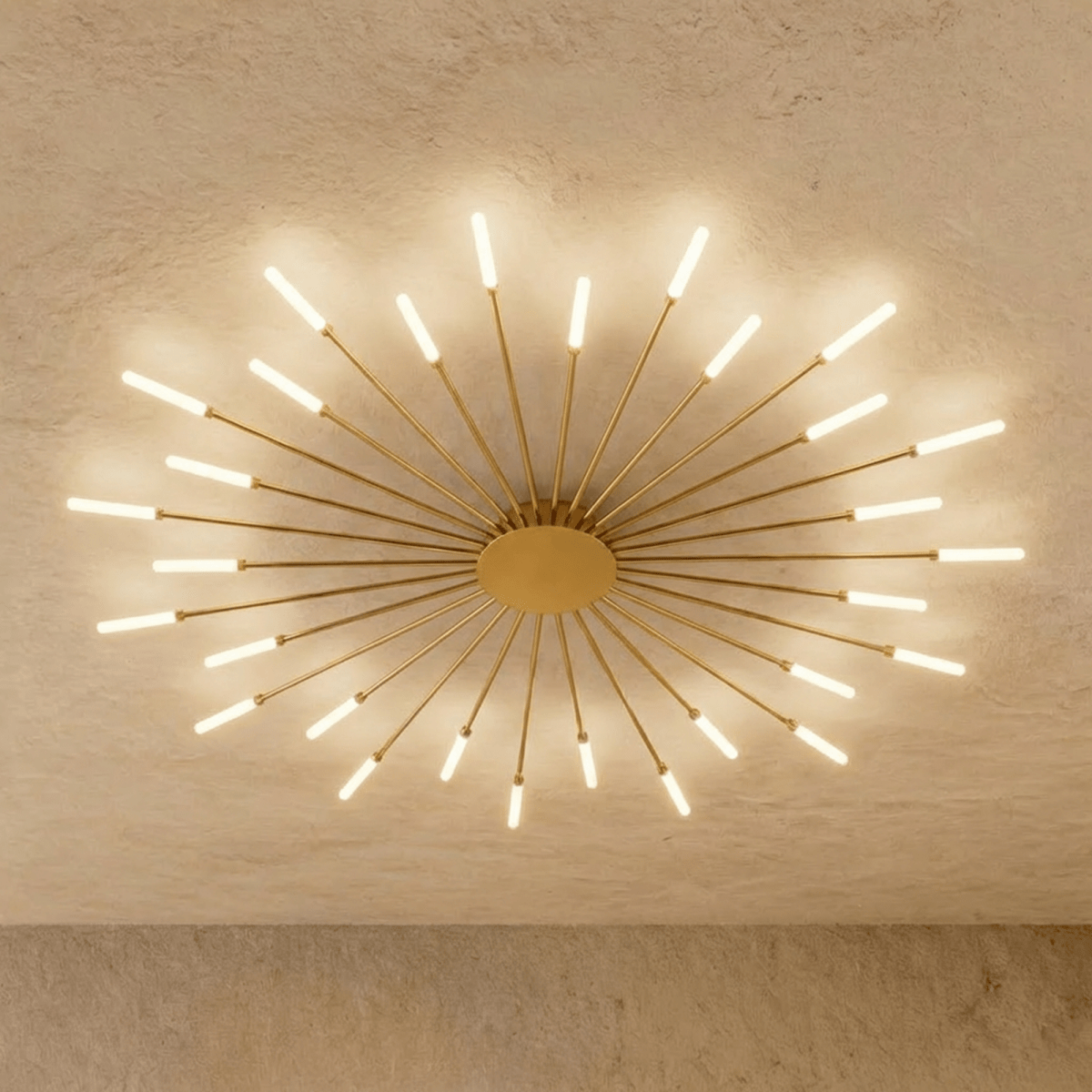 Clérachic starburst chandelier in gold, the dense even ring casting overlapping fans of light across the plaster.
