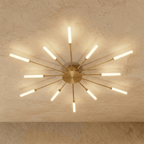 Clérachic starburst chandelier in gold, the same twelve arms, each rod catching the light from its tube.