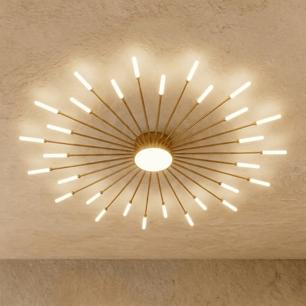 Clérachic starburst chandelier in gold, the dense even ring, its rods crowding the drum above a glowing disc.