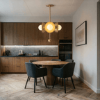 Clérachic brass disc-and-globe pendant light lit above a round table in a walnut-cabinet kitchen dining area.