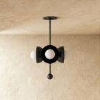 Clérachic disc-and-globe pendant light in matte black, shown from a slightly closer studio angle on a plaster wall.