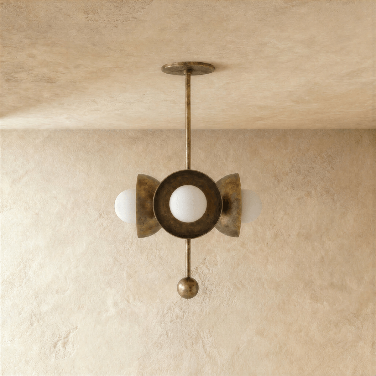Clérachic disc-and-globe pendant light in vintage brass, shown from a slightly closer studio angle on a plaster wall.