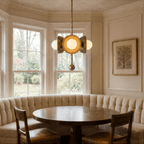 Clérachic vintage brass disc-and-globe pendant light lit above a round table in a curtained bay-window nook.