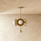 Clérachic disc-and-globe pendant light in polished brass, shown from a slightly closer studio angle on a plaster wall.
