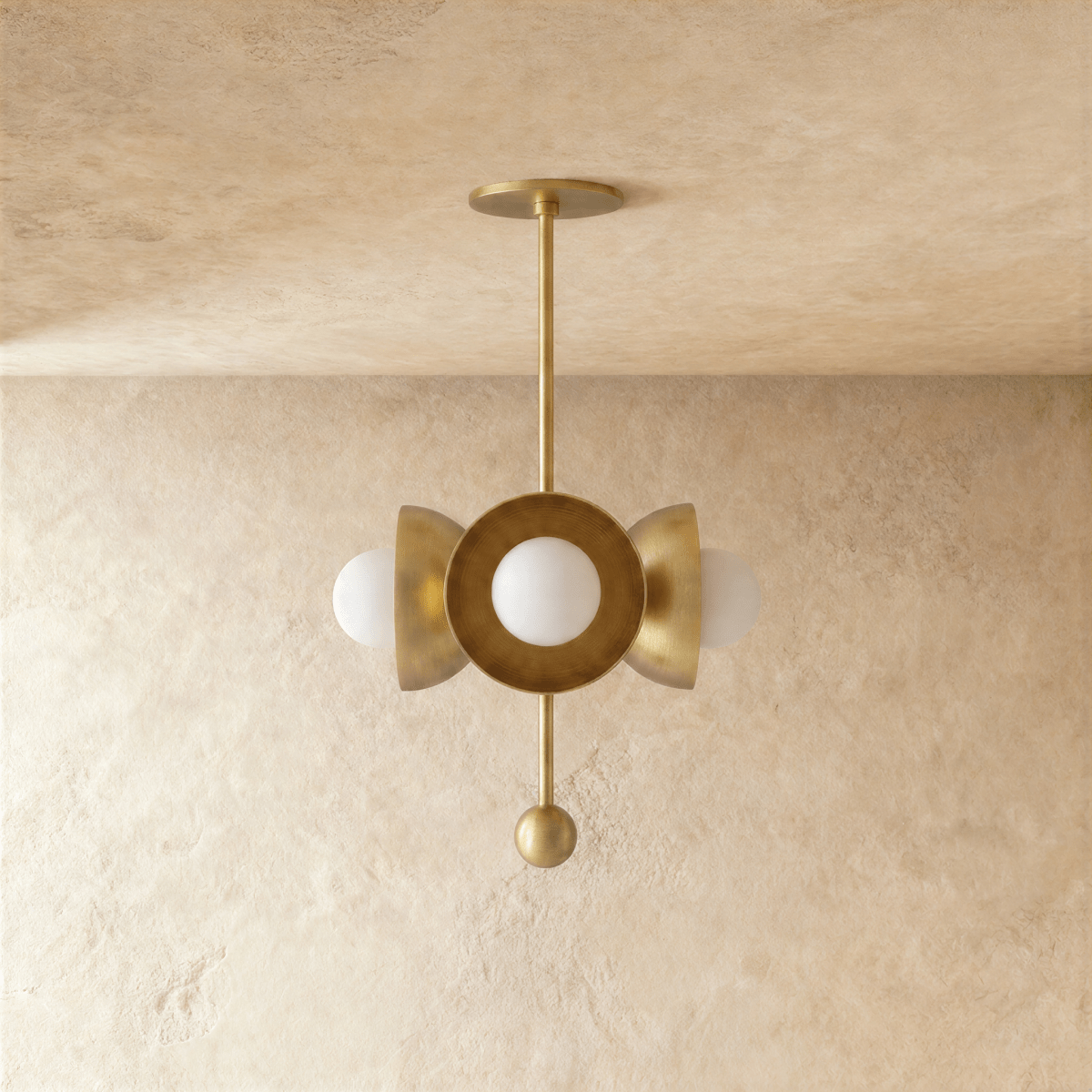 Clérachic disc-and-globe pendant light in polished brass, shown from a slightly closer studio angle on a plaster wall.