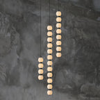 Orbique pendants in three lengths glowing side by side against a dark textured concrete wall