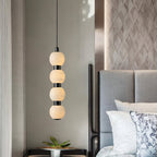 Four-ball Orbique pendant lit beside a grey upholstered headboard and a bedside table