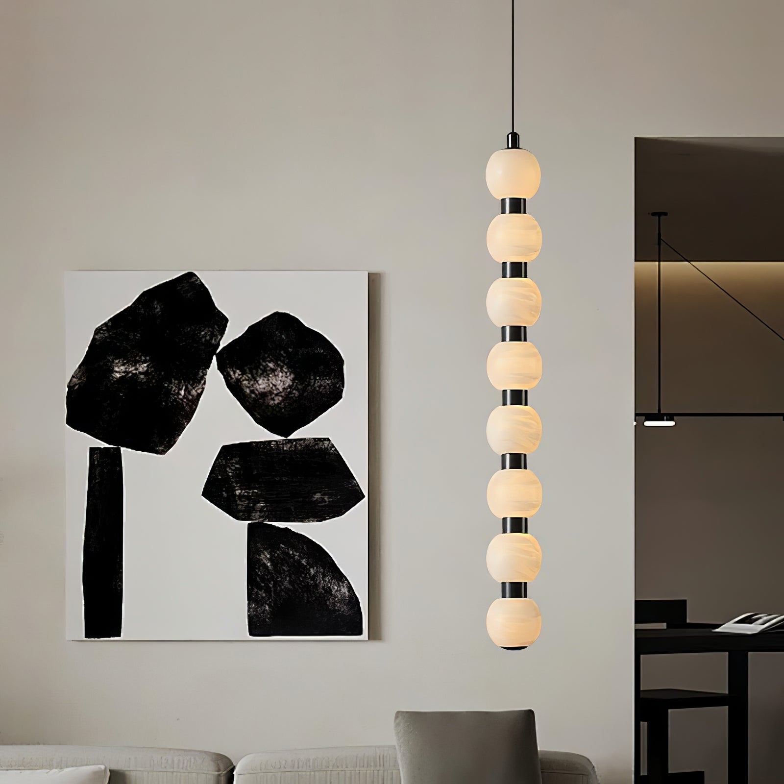 Eight-ball Orbique pendant lit beside a black and white canvas above a pale living room sofa