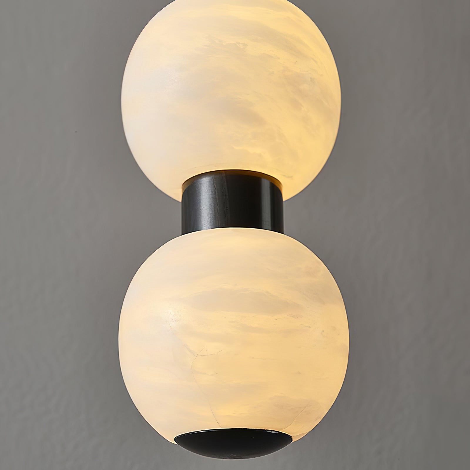 Extreme close-up of two lit alabaster spheres and the black metal collar that joins them