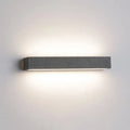 Charcoal cement wall lamp lit head-on, washing warm light up and down the wall above and below it.