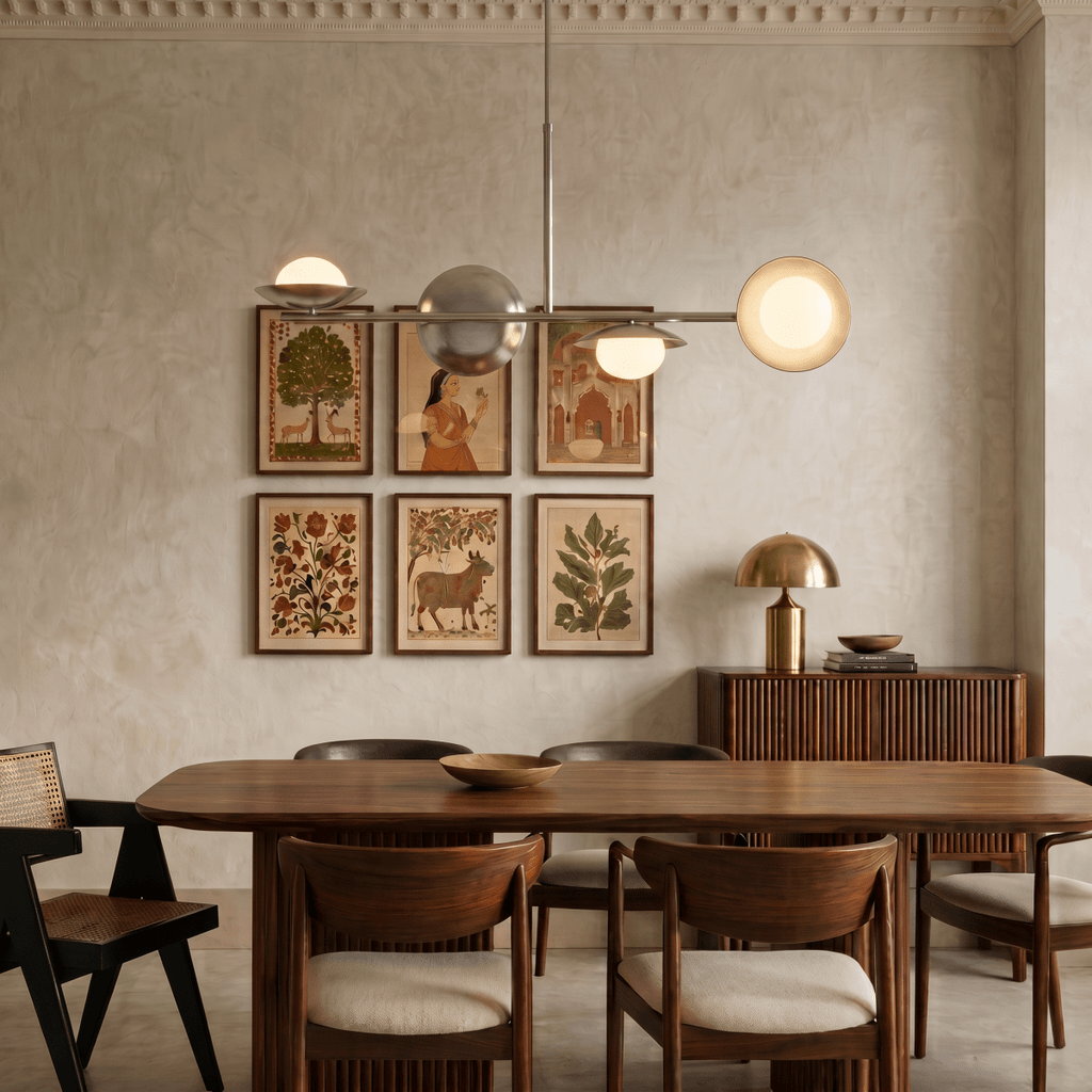 Clérachic chrome pendant light suspended above a dining table, beside a wall of framed folk-art prints in a plaster room.