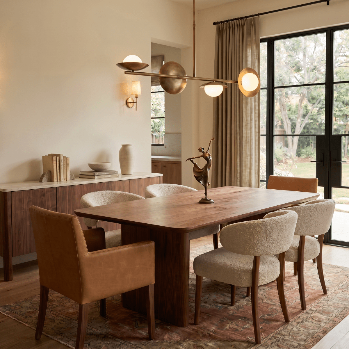 Clérachic vintage brass pendant light glowing above a wood dining table beside a gallery wall of framed art prints.