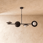 Clérachic pendant light in matte black, the linear bar with round discs and glass globes seen from the side.