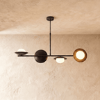 Clérachic pendant light in matte black, its sculptural spheres and opal glass globes lit against a plaster ceiling.