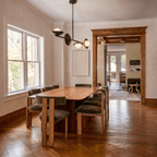 Clérachic matte black pendant light hanging above a long dining table on a herringbone wood floor near tall windows.