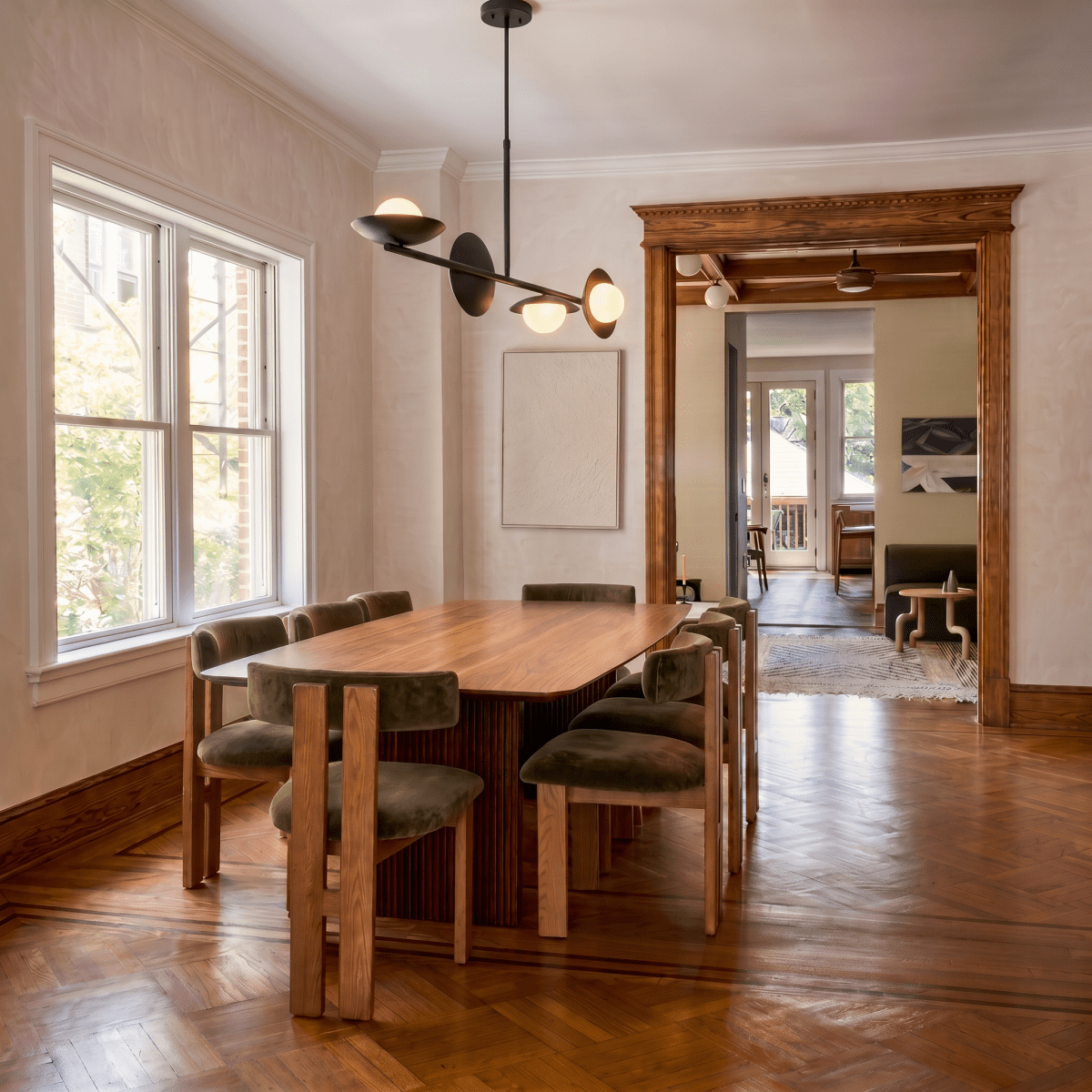 Clérachic matte black pendant light hanging above a long dining table on a herringbone wood floor near tall windows.