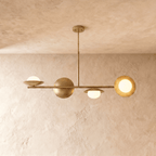 Clérachic pendant light in a brighter brass finish, its spheres and opal globes suspended below a plaster ceiling.