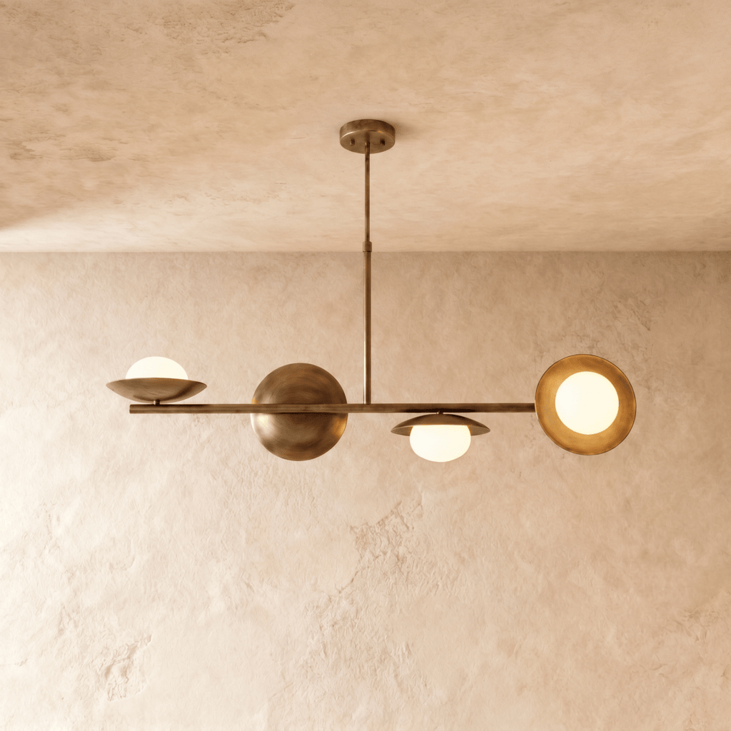Clérachic pendant light in vintage brass, its sculptural spheres and opal glass globes lit against a plaster ceiling.