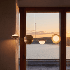 Clérachic vintage brass pendant light silhouetted against a sunset view over water through a timber-framed window.