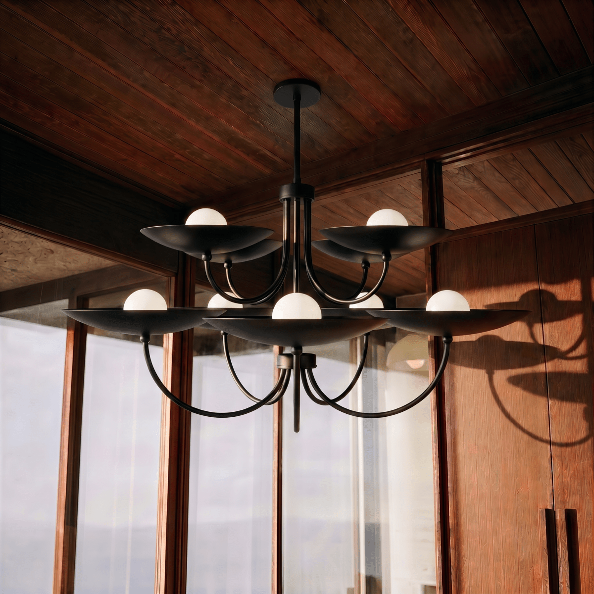 Clérachic matte black two-tier disc chandelier lit in a wood-panelled sunroom overlooking a mountain view.