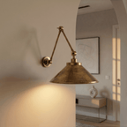 This vintage brass Clérachic wall lamp lights an archway leading to a console table and framed art.
