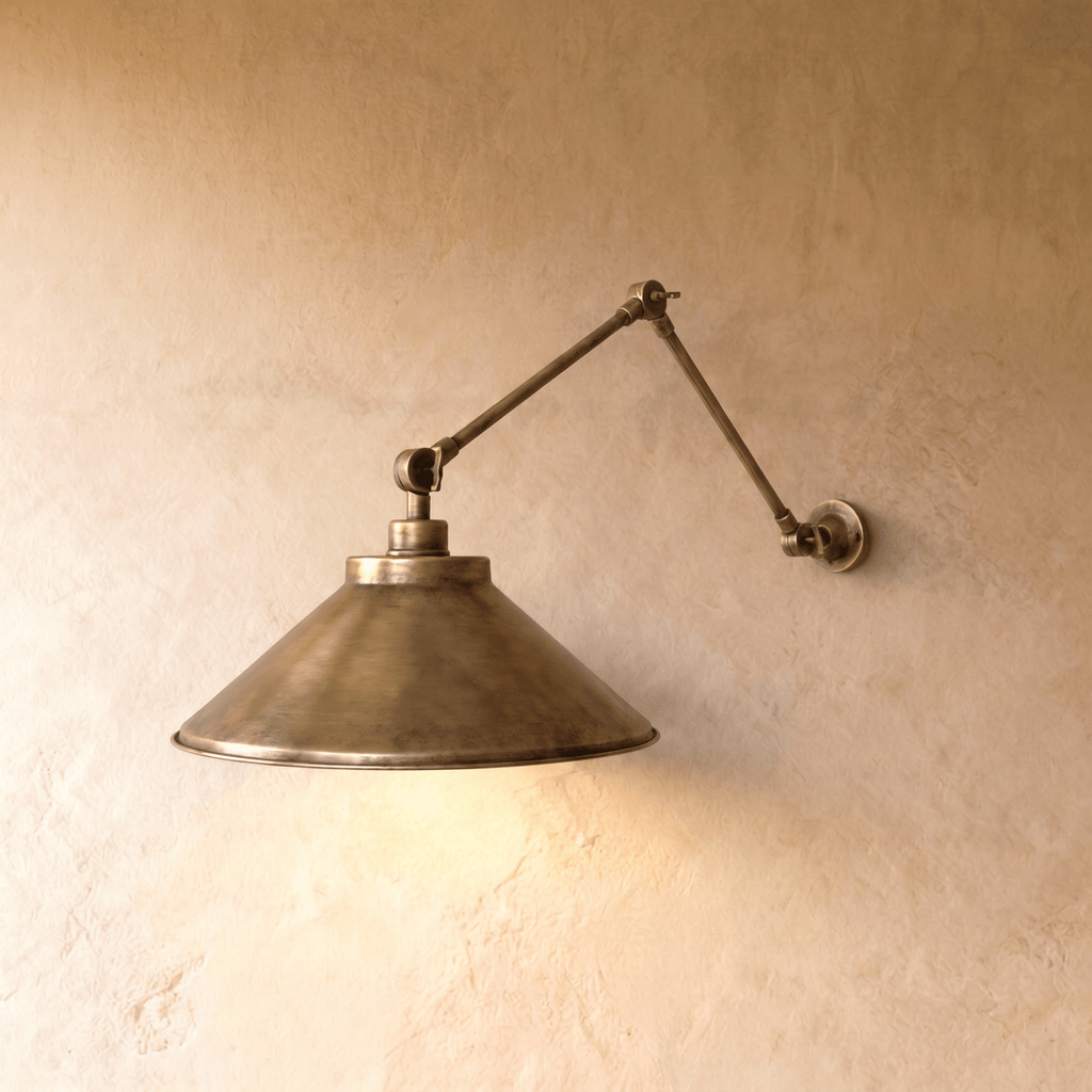 Clérachic wall lamp in vintage brass with a wide cone shade on a double-jointed swing arm against a plaster wall.
