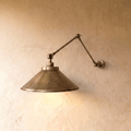Clérachic wall lamp in vintage brass with a wide cone shade on a double-jointed swing arm against a plaster wall.