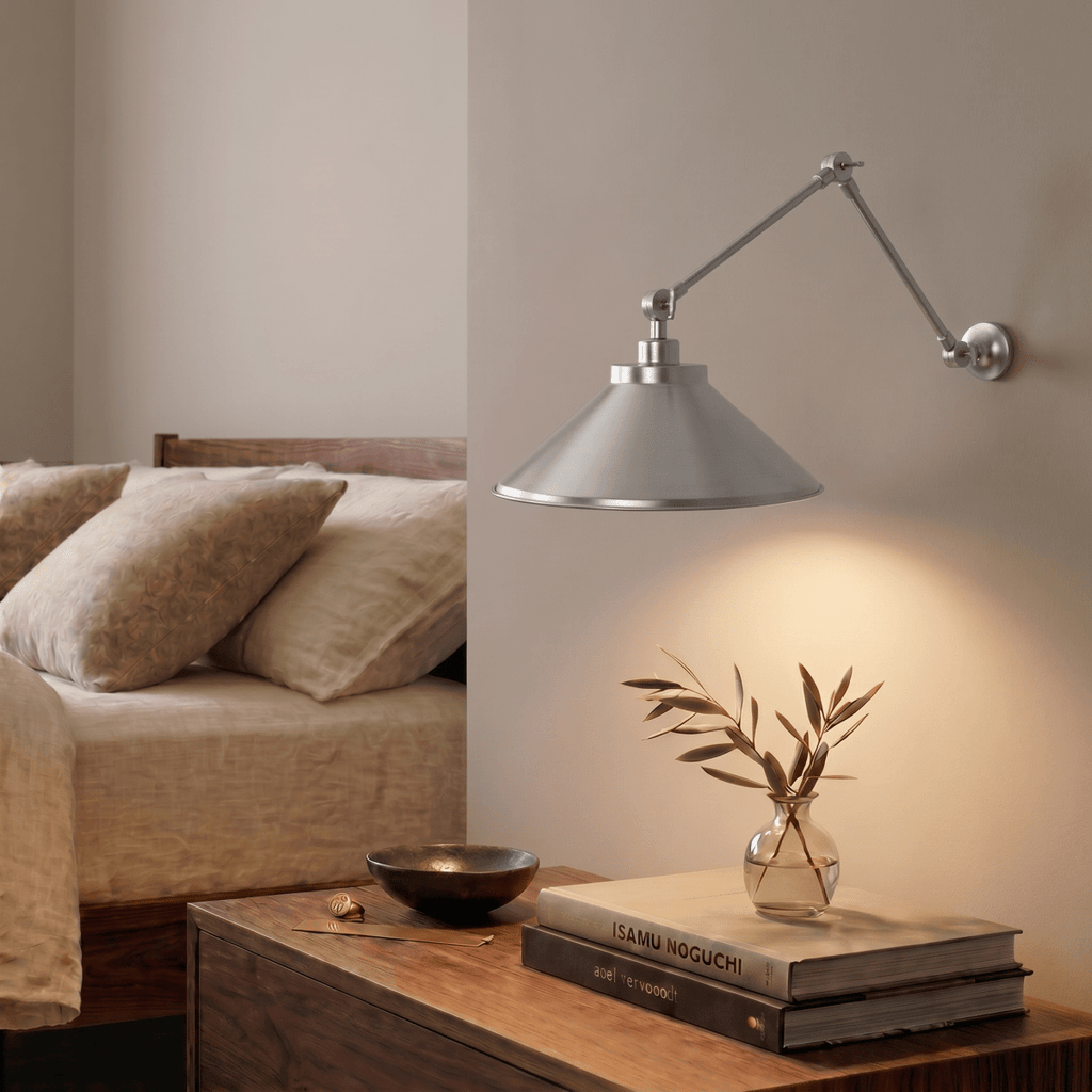 A chrome Clérachic wall lamp lights a walnut nightstand holding olive branches and stacked books.