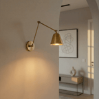 A Clérachic swing-arm wall light in aged vintage brass lights a plastered archway leading into a living space.