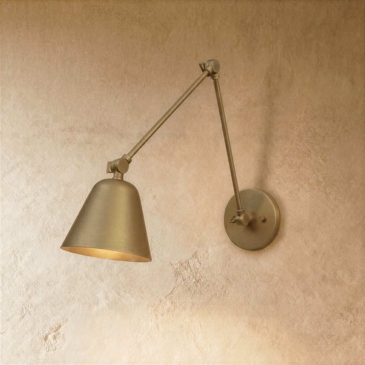 A Clérachic swing-arm wall light in polished brass catches the light on its cone shade against a plaster wall.