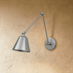 A Clérachic wall light in brushed chrome shows its jointed swing arm reaching left with the shade tilted down.
