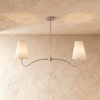Clérachic double-arm chandelier in a bright chrome finish, its linen cone shades hung from a plaster ceiling.