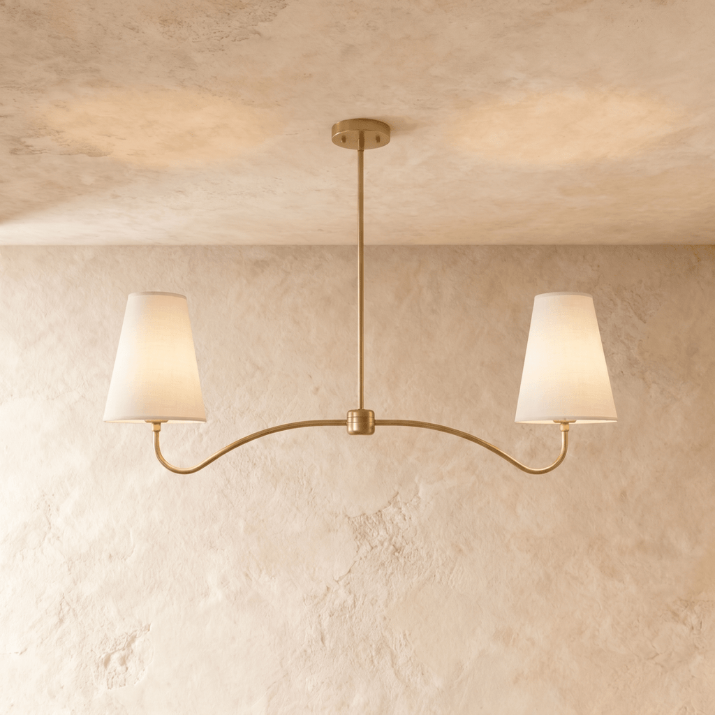 Clérachic double-arm chandelier in a brighter brass finish, its linen cone shades hung from a plaster ceiling.