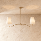 Clérachic double-arm chandelier in a brighter brass finish, its linen cone shades hung from a plaster ceiling.