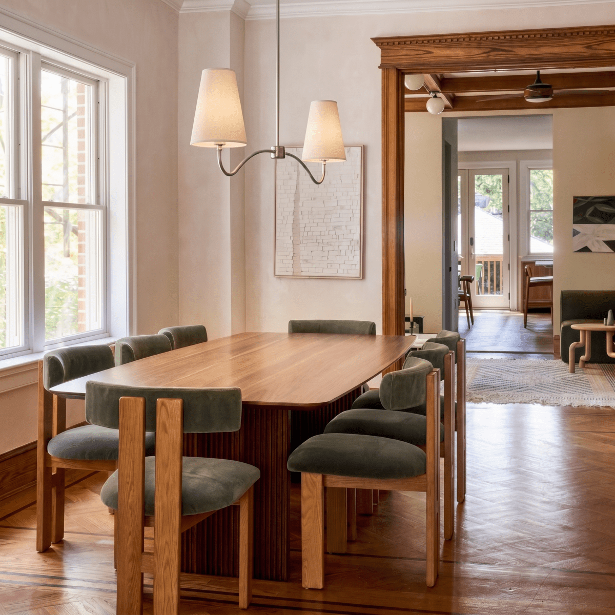 Clérachic chrome chandelier hanging above a herringbone-floored dining table near tall black-framed windows.