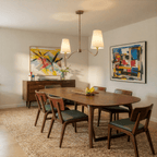 Clérachic vintage brass chandelier glowing above a walnut dining table flanked by two colourful abstract paintings.
