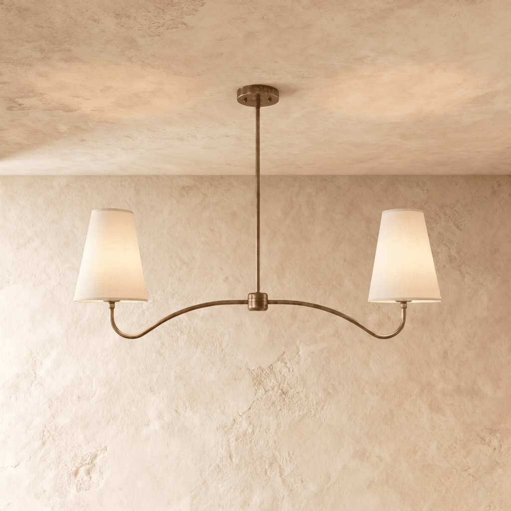Clérachic double-arm chandelier in vintage brass, its linen cone shades hung from a plaster ceiling.