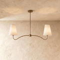 Clérachic double-arm chandelier in vintage brass, its linen cone shades hung from a plaster ceiling.