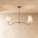 Clérachic double-arm chandelier in vintage brass, its linen cone shades hung from a plaster ceiling.