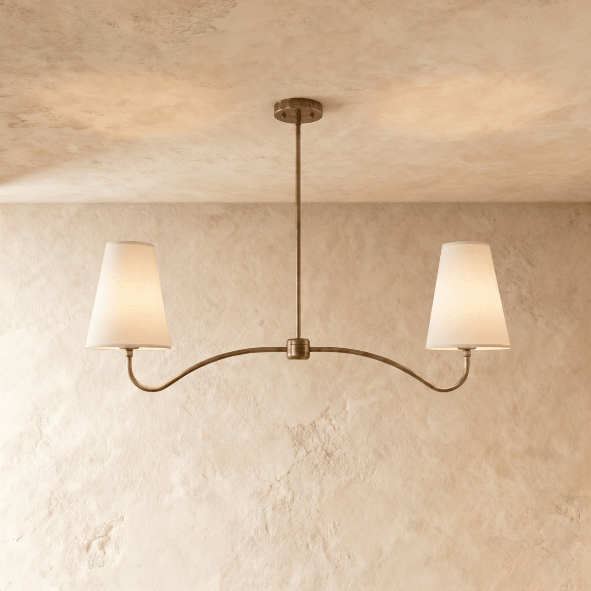Clérachic double-arm chandelier in vintage brass, its linen cone shades hung from a plaster ceiling.